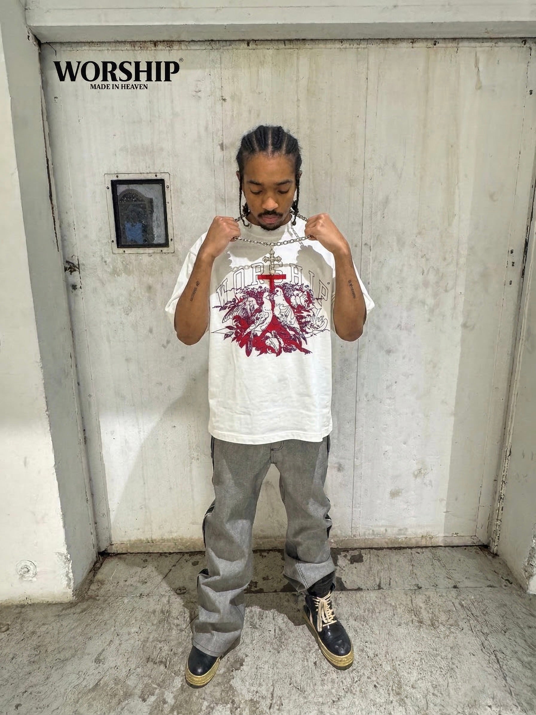 Person wearing a white t-shirt with a red design in front of a concrete wall with 'WORSHIP' branding.